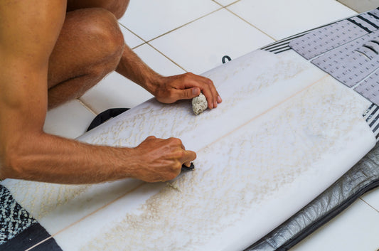 a person maintaining their surfboard by cleaning it