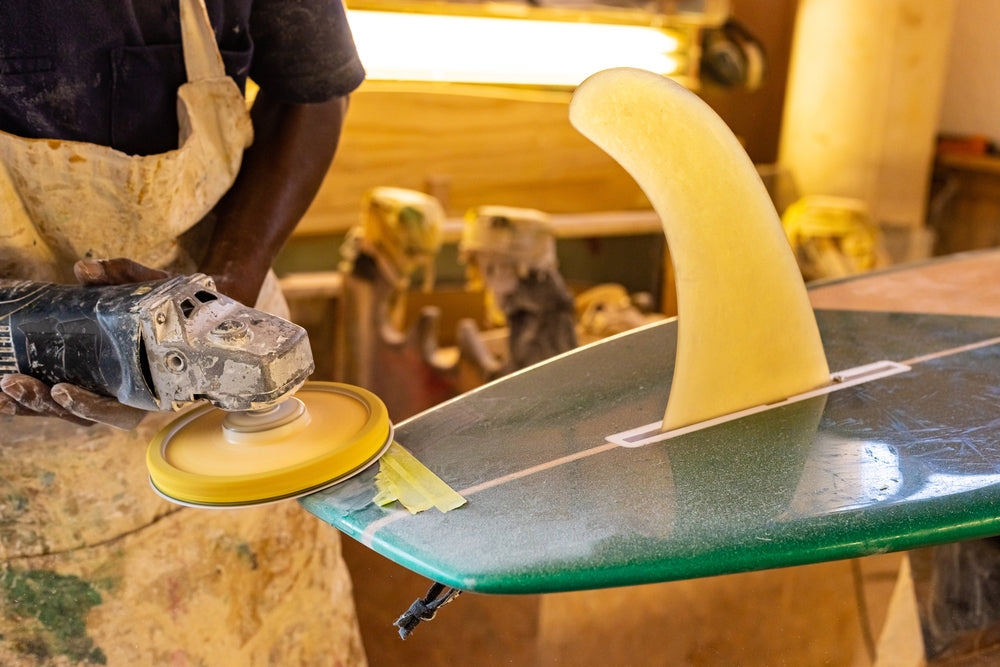 a man with a power tool pollishing a handmade surfboard