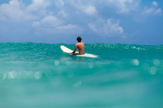 unidentified man on surf board waite for wave in blue ocean water back view